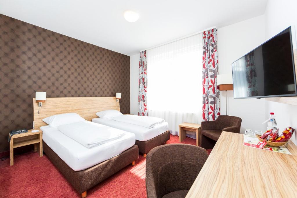 Ljust och modernt dubbelrum på Hotel Lenz i Fulda, Tyskland, med två sängar, skrivbord, platt-TV och sittgrupp.